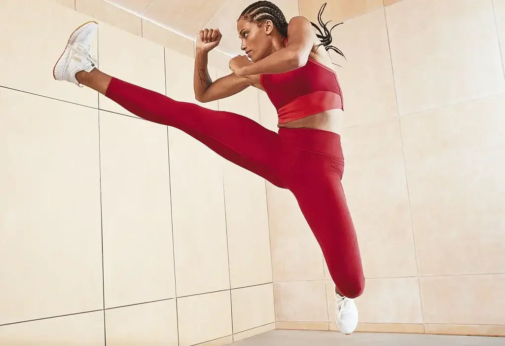 Woman in red sports bra and leggings doing high kick in gym, showcasing activewear