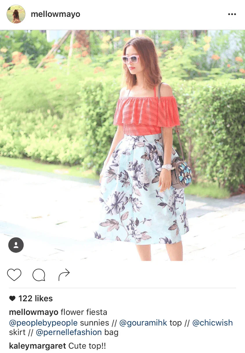 Woman in a red off-shoulder top and floral print skirt outdoors, wearing sunglasses.
