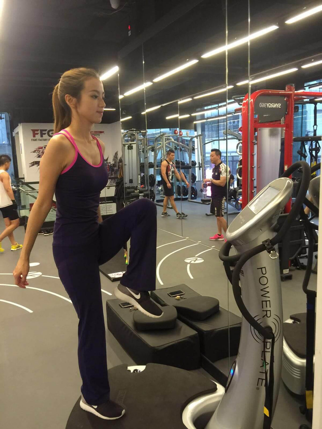 Woman in activewear exercising on Power Plate machine in modern gym environment