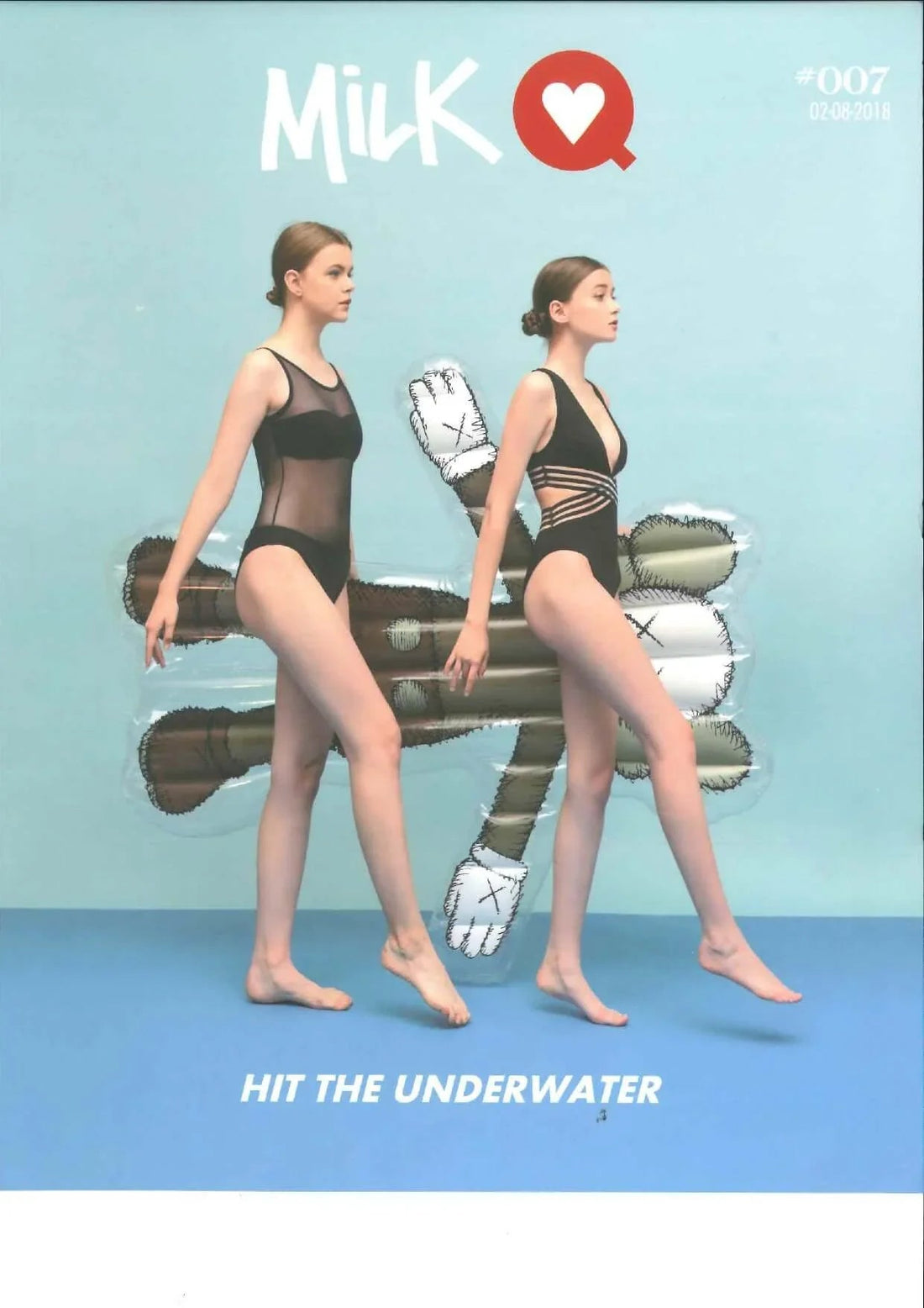 Two women in stylish black swimsuits walking by pool with inflatable float on blue background