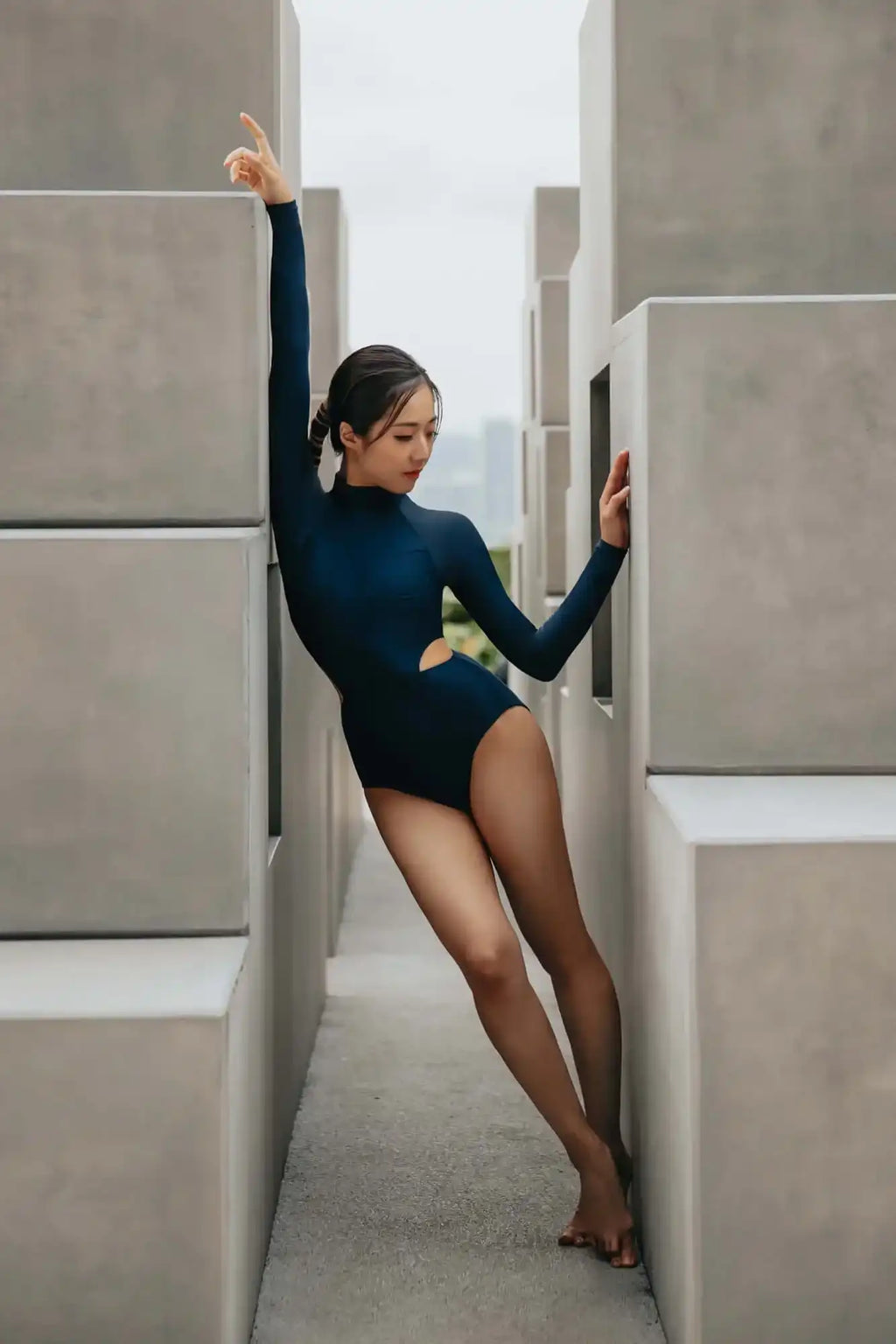 "一名身穿海军蓝长袖连体泳衣的女性，在现代混凝土墙之间摆姿势拍照"