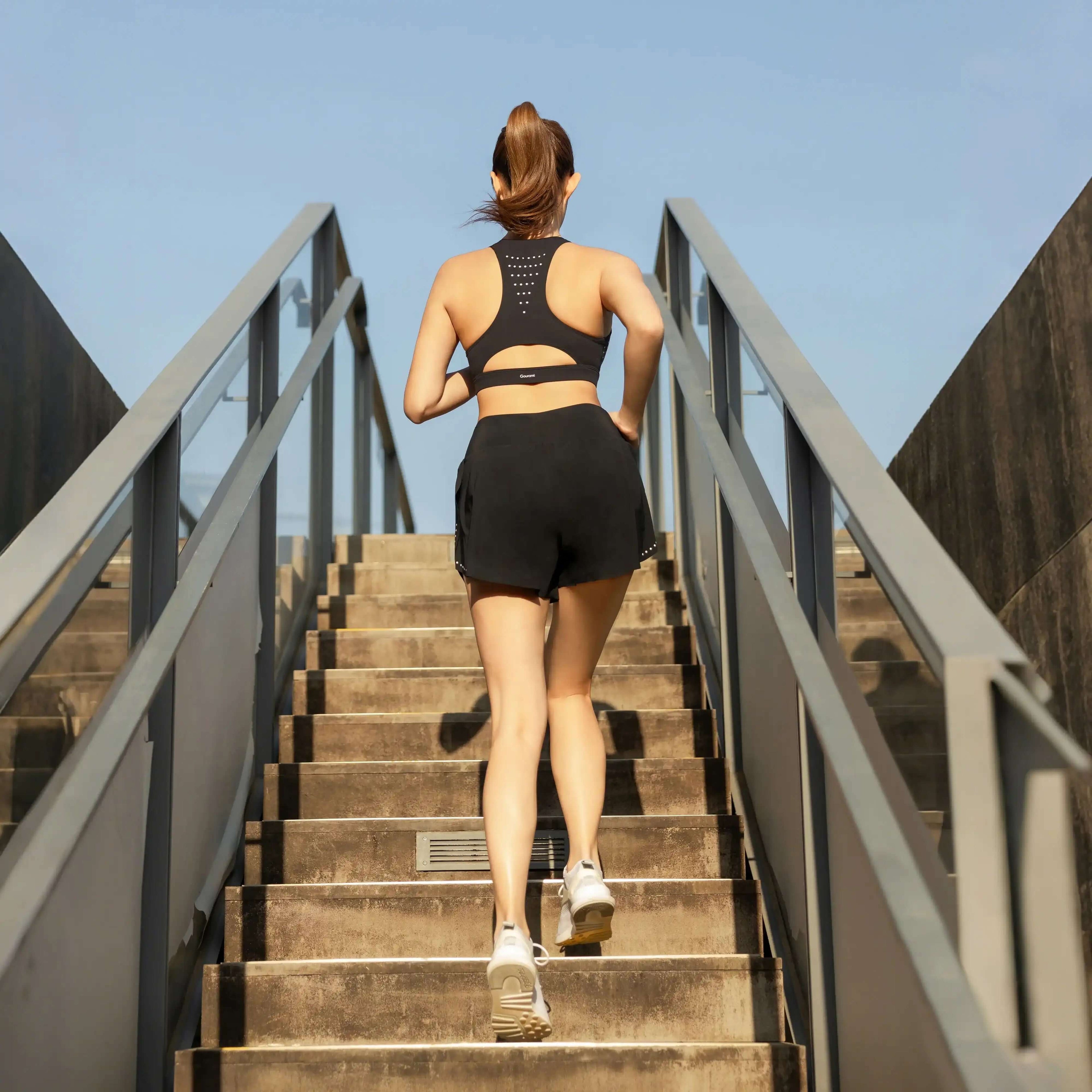 Woman in high-performance activewear running up outdoor stairs, sporty fitness scene