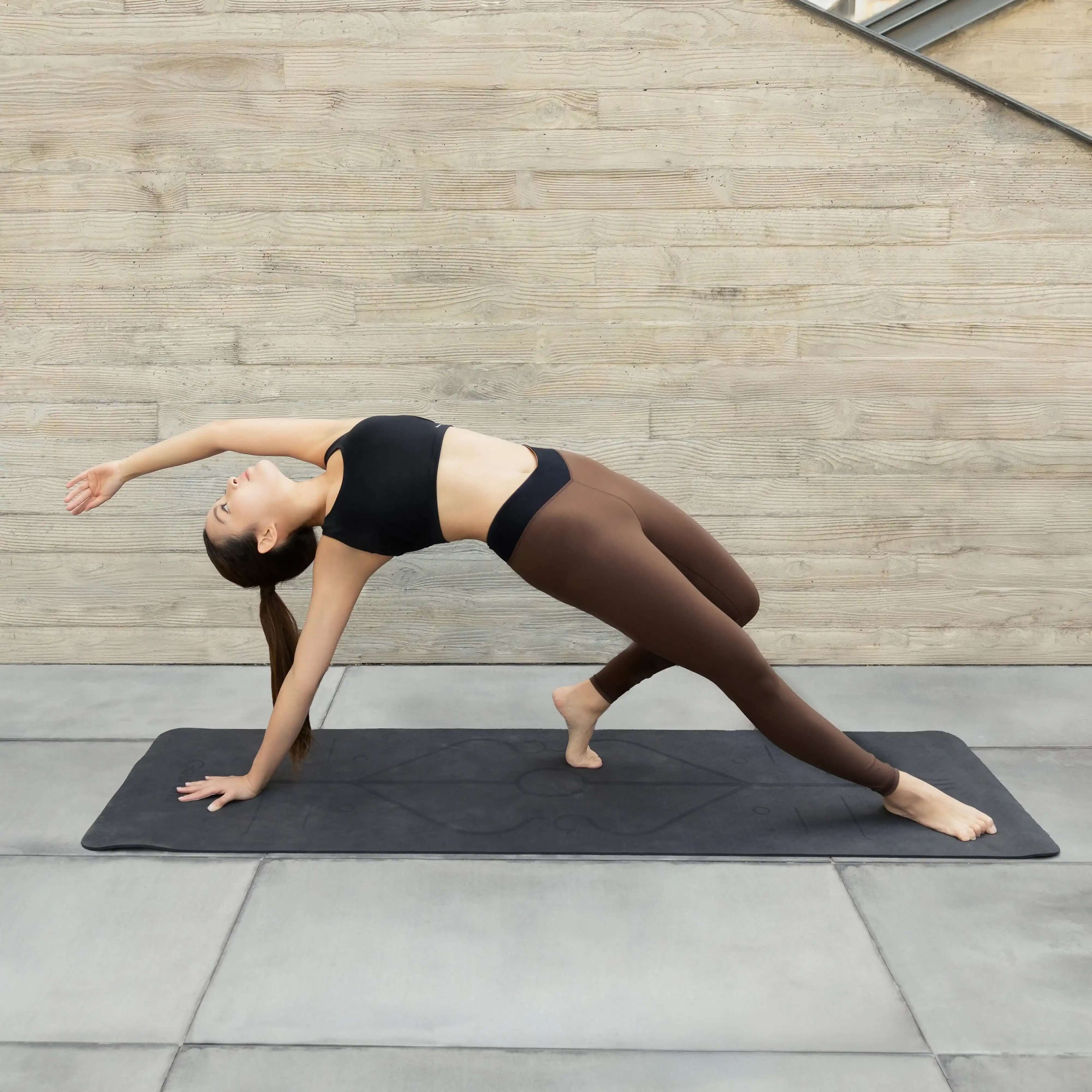 Woman in black crop top and brown leggings doing yoga on a mat in modern activewear