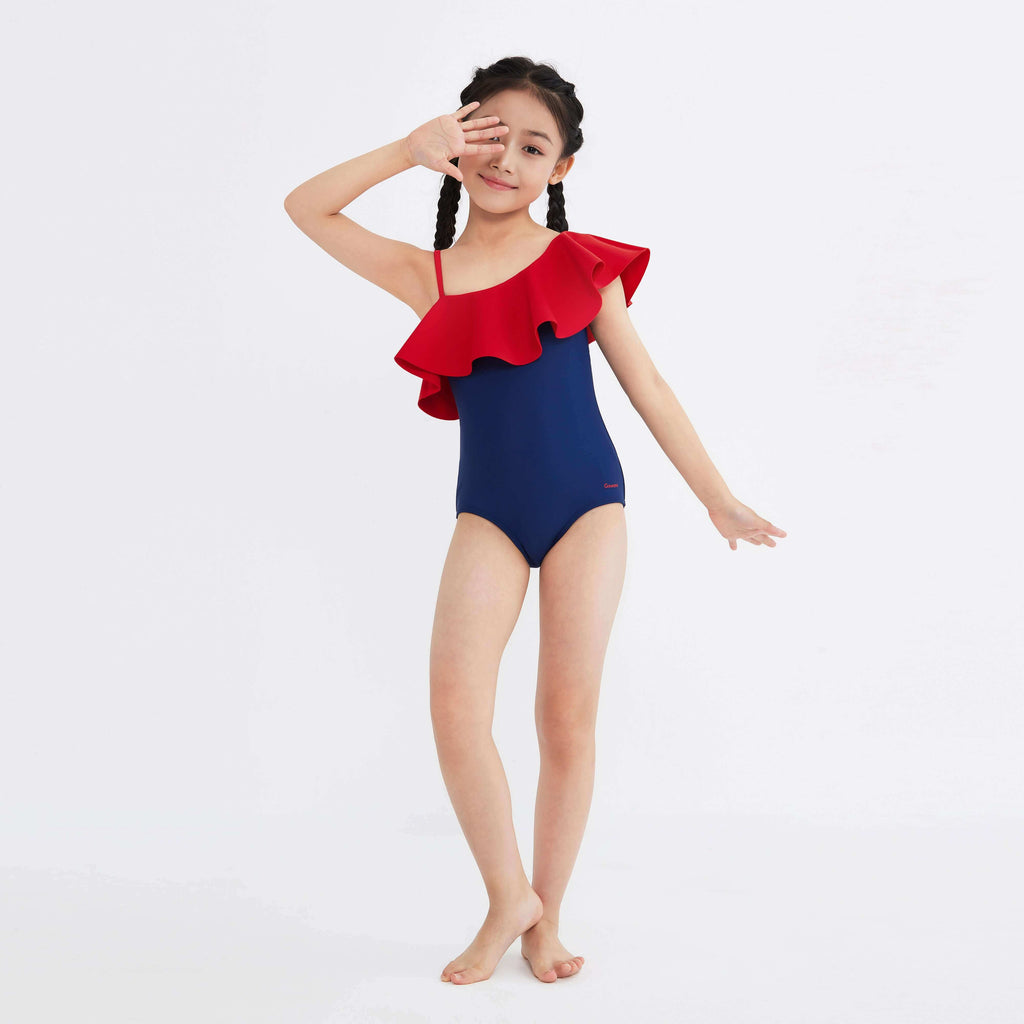 Girl in navy one-piece swimsuit with red ruffle shoulder detail, posing playfully against white background.