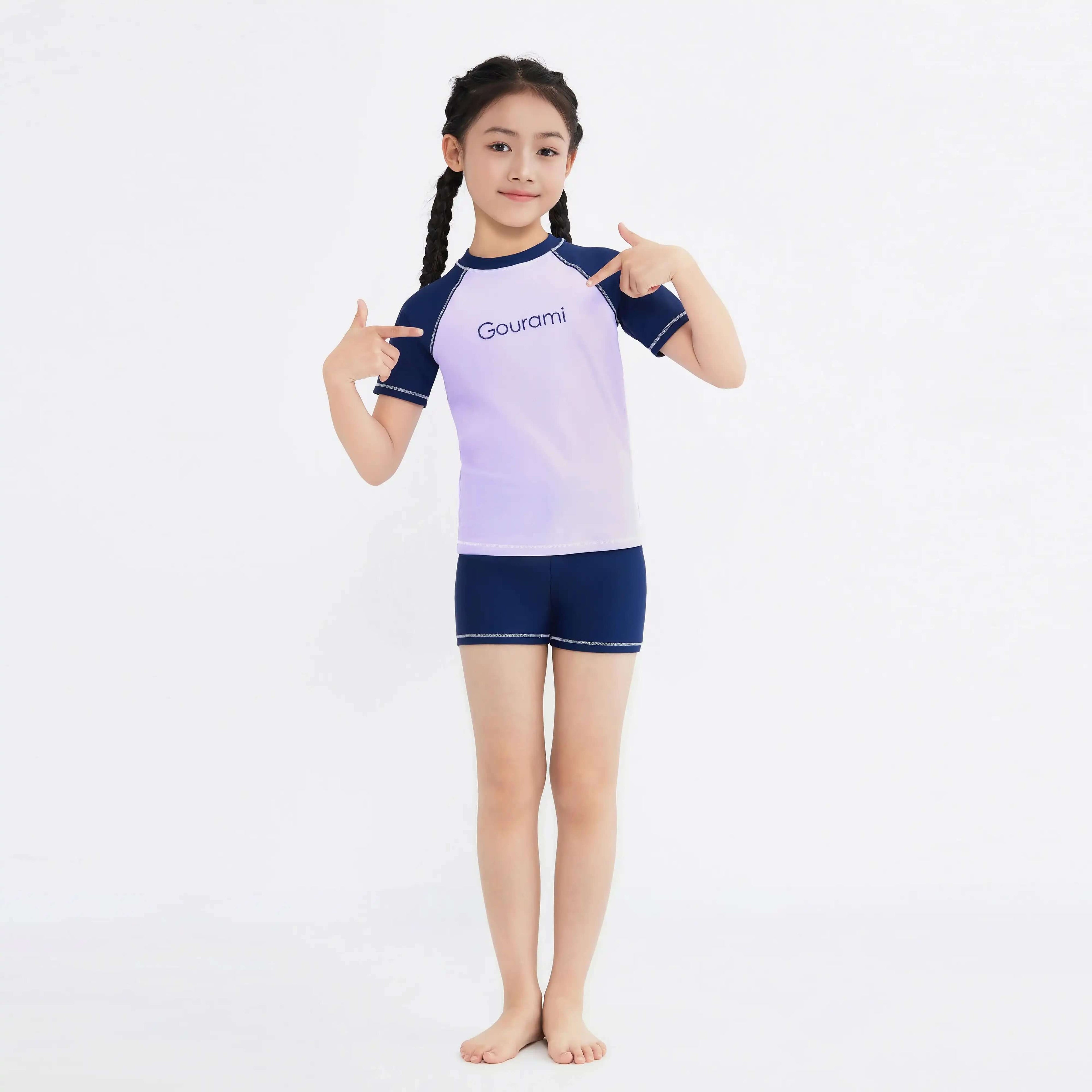 Girl in Gourami purple and navy swimwear set, pointing to logo, ideal for active beach days.