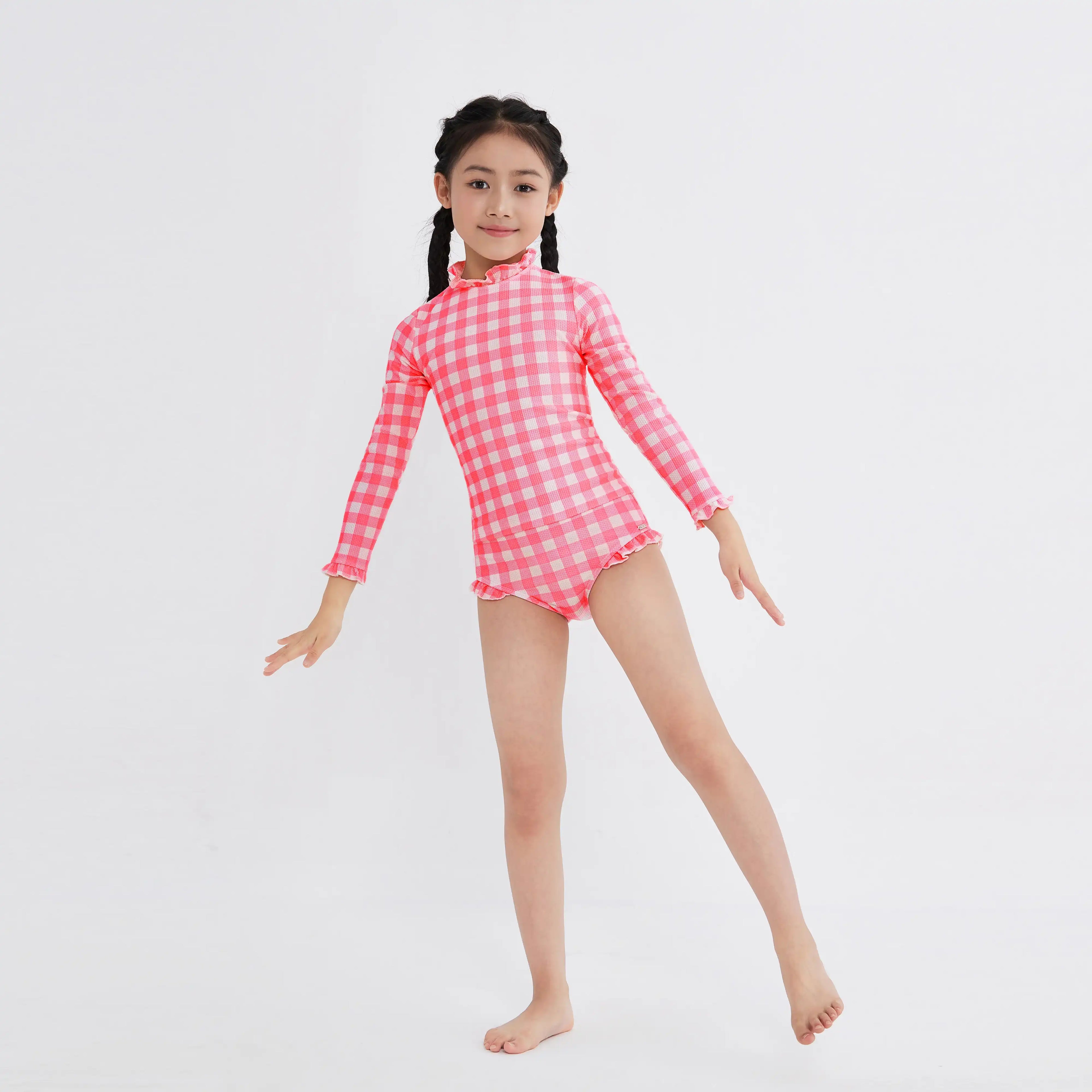 Girl in pink and white gingham one-piece swimsuit with ruffles, long sleeves, and high neck for sun protection.
