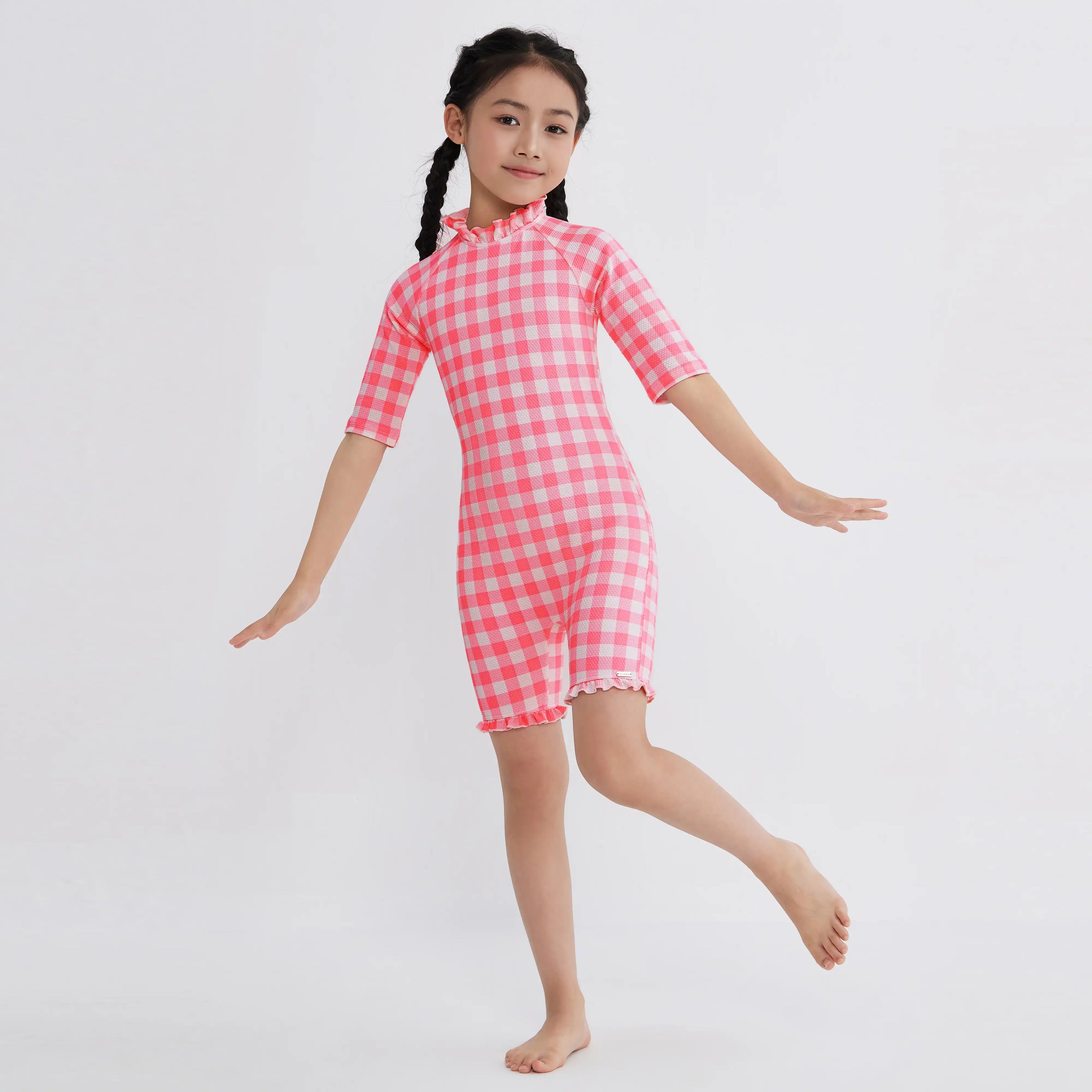 Girl in pink and white gingham one-piece swimsuit with ruffles, perfect for kids' swimwear.