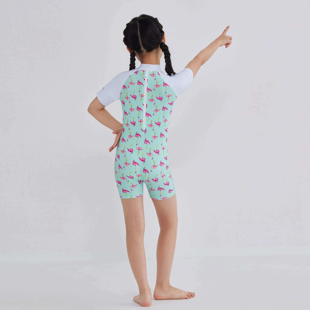 Girl in flamingo print swim rash guard with short sleeves and back zipper, pointing forward