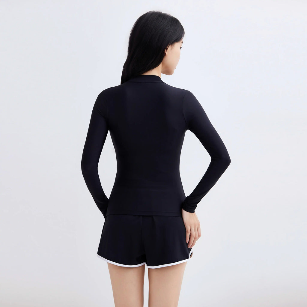 Rear view of a woman wearing a black long-sleeve Swim Fit multi-purpose swim jacket and shorts.