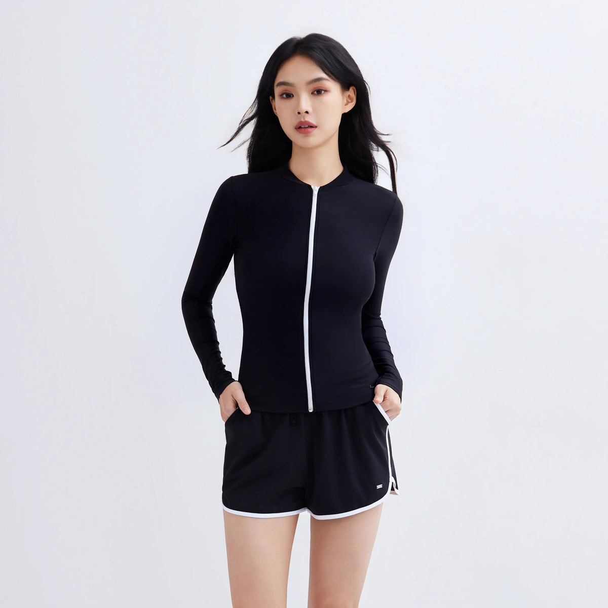 Woman wearing a black multi-purpose swim jacket with white zip and matching swim shorts.