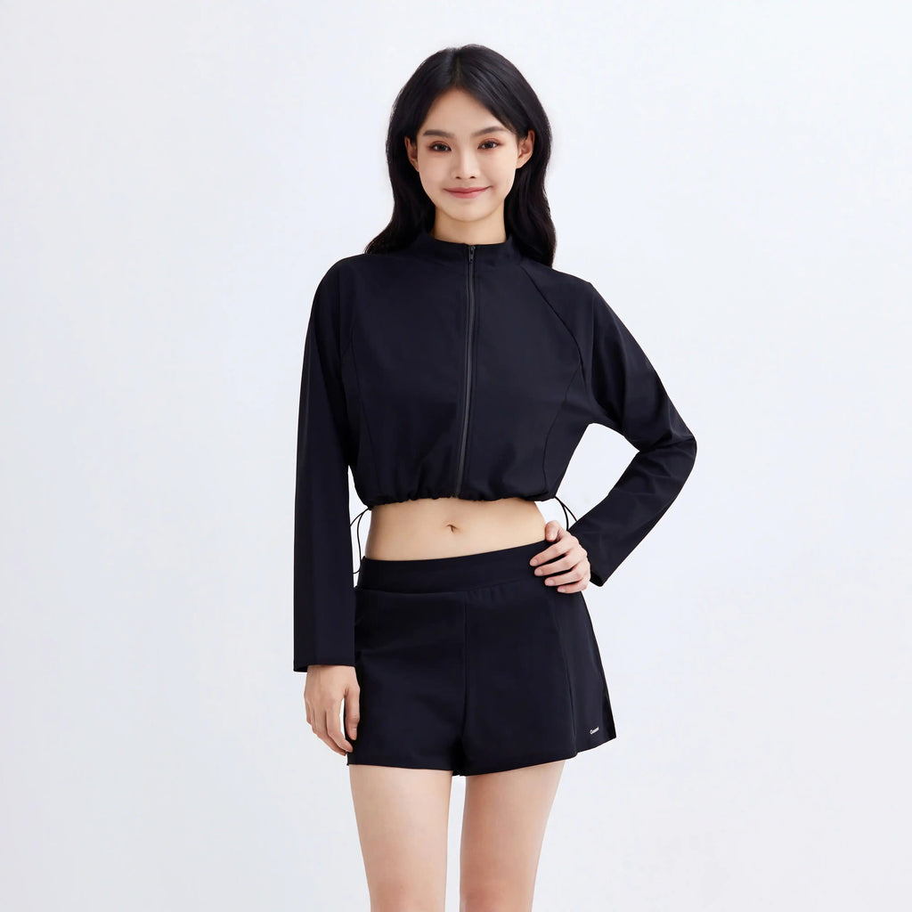 Woman wearing Gourami black Drift Gym To Swim cropped zip-up jacket and matching shorts.