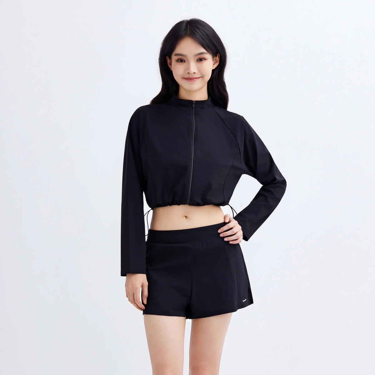 Woman wearing Gourami black Drift Gym To Swim cropped zip-up jacket and matching shorts.