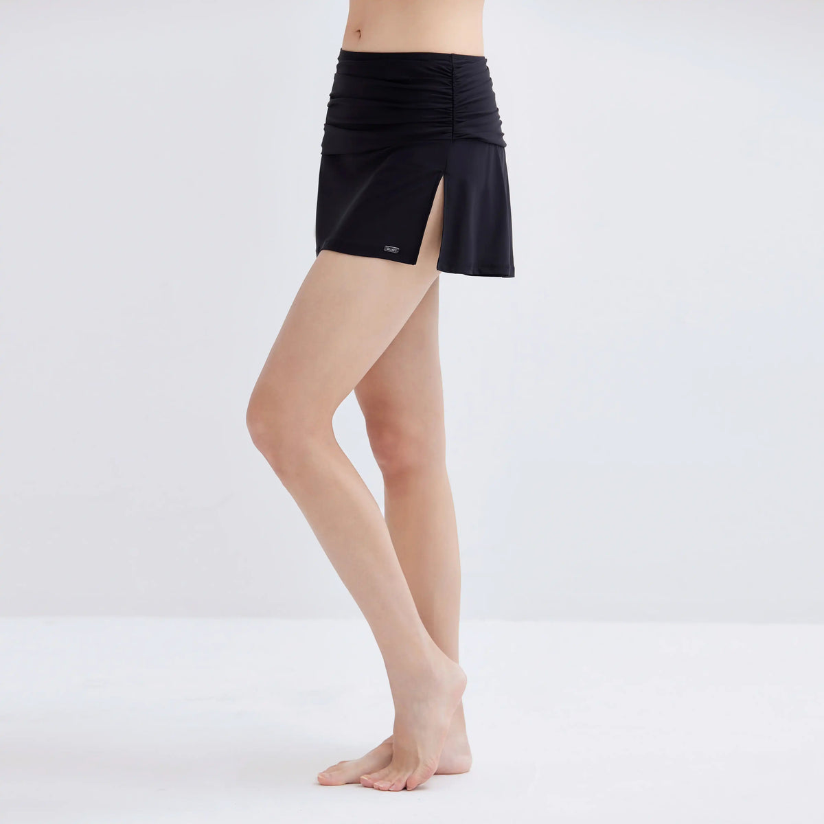Woman wearing a black Gourami Tuck Swim Skirt with ruching and a side slit.
