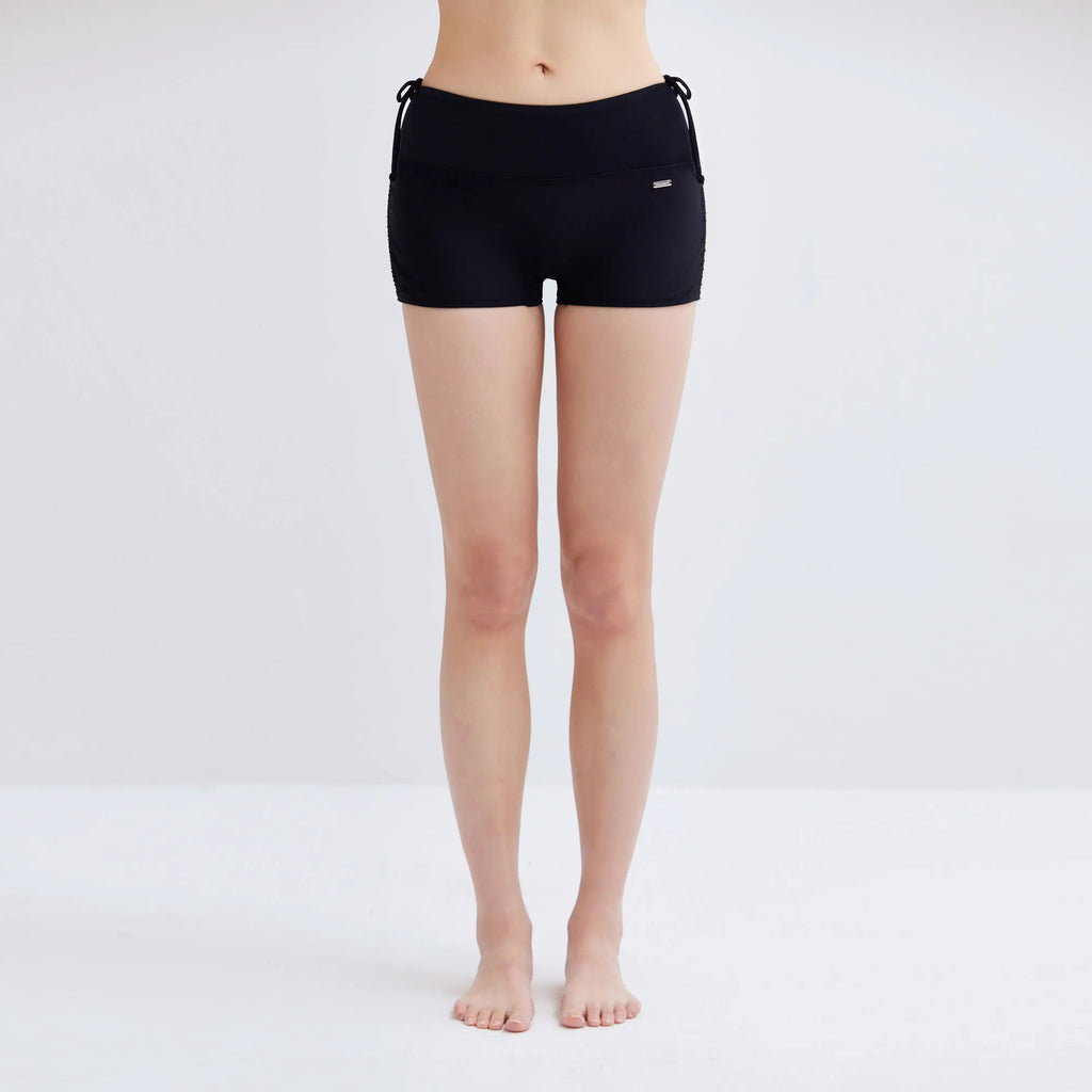 Woman wearing black Swim Fit Ladies Scrunchie Shorts against a white background.