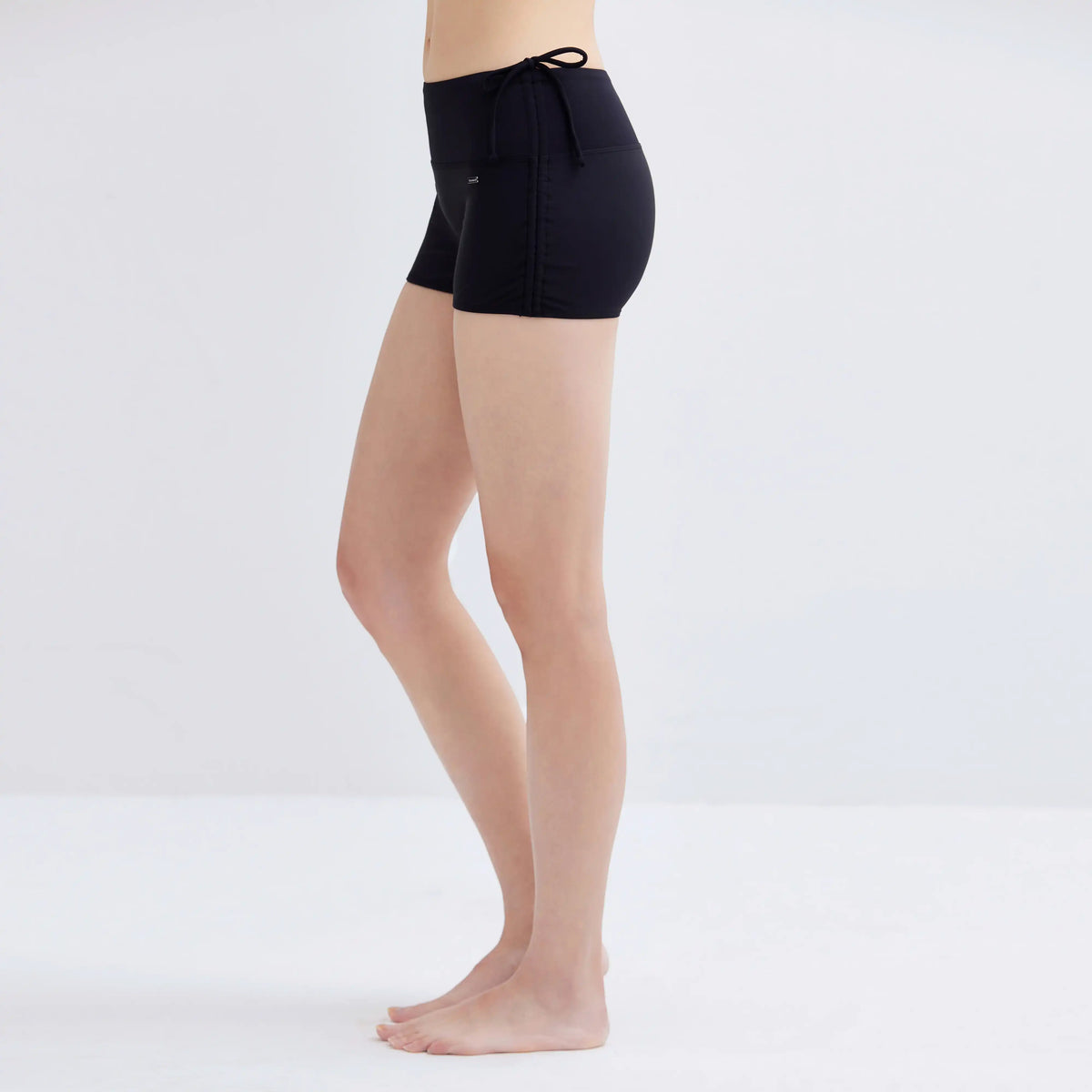 Side view of a woman wearing black Swim Fit Ladies Scrunchie Shorts.