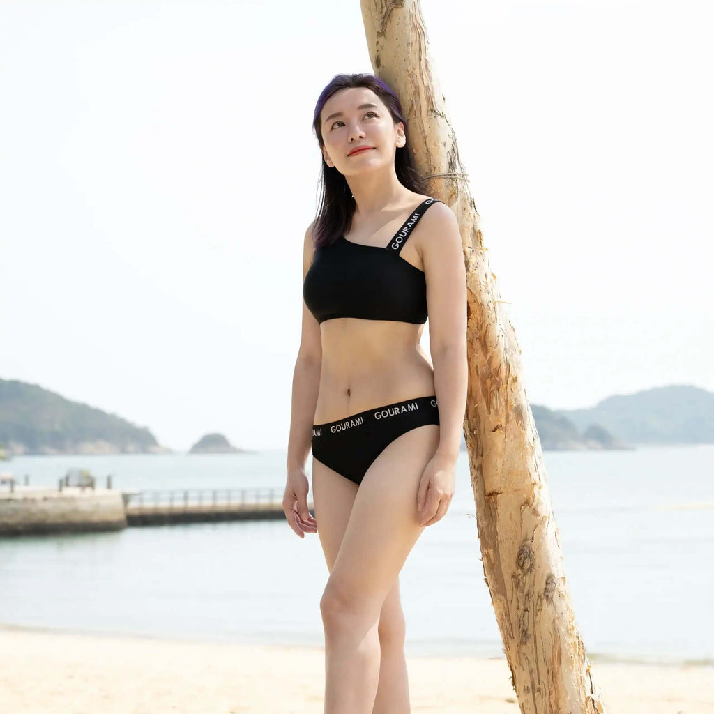 一位模特在海滩上展示古拉米乐队女士比基尼，背景是风景如画的水景。