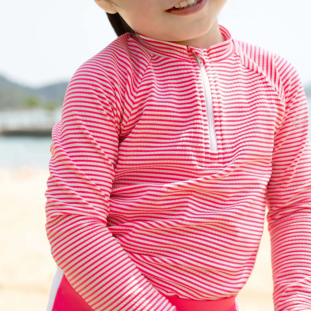 Candy Stripe Girls Rashguard Set worn by a child at the beach, featuring vibrant pink stripes.
