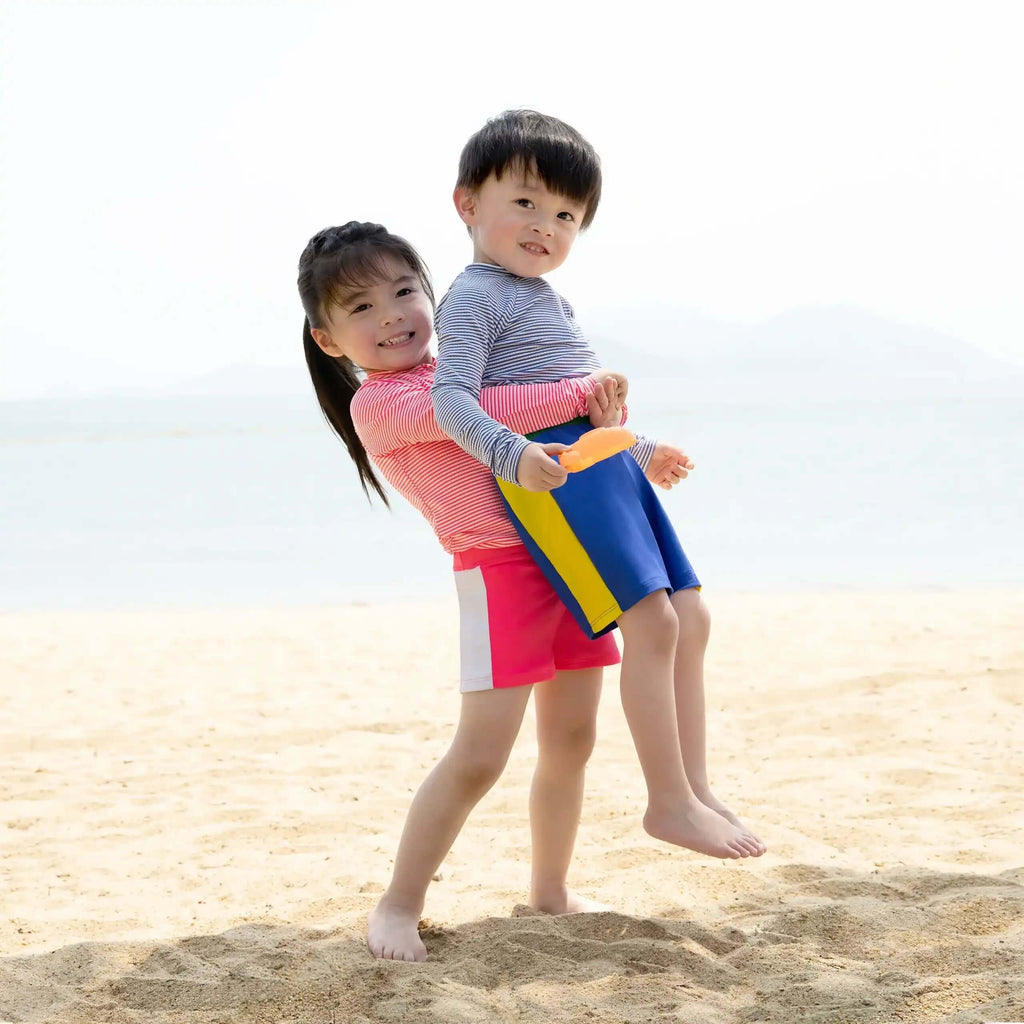Children playing on the beach wearing Candy Stripe Boys Rashguard Set and colorful swim shorts.