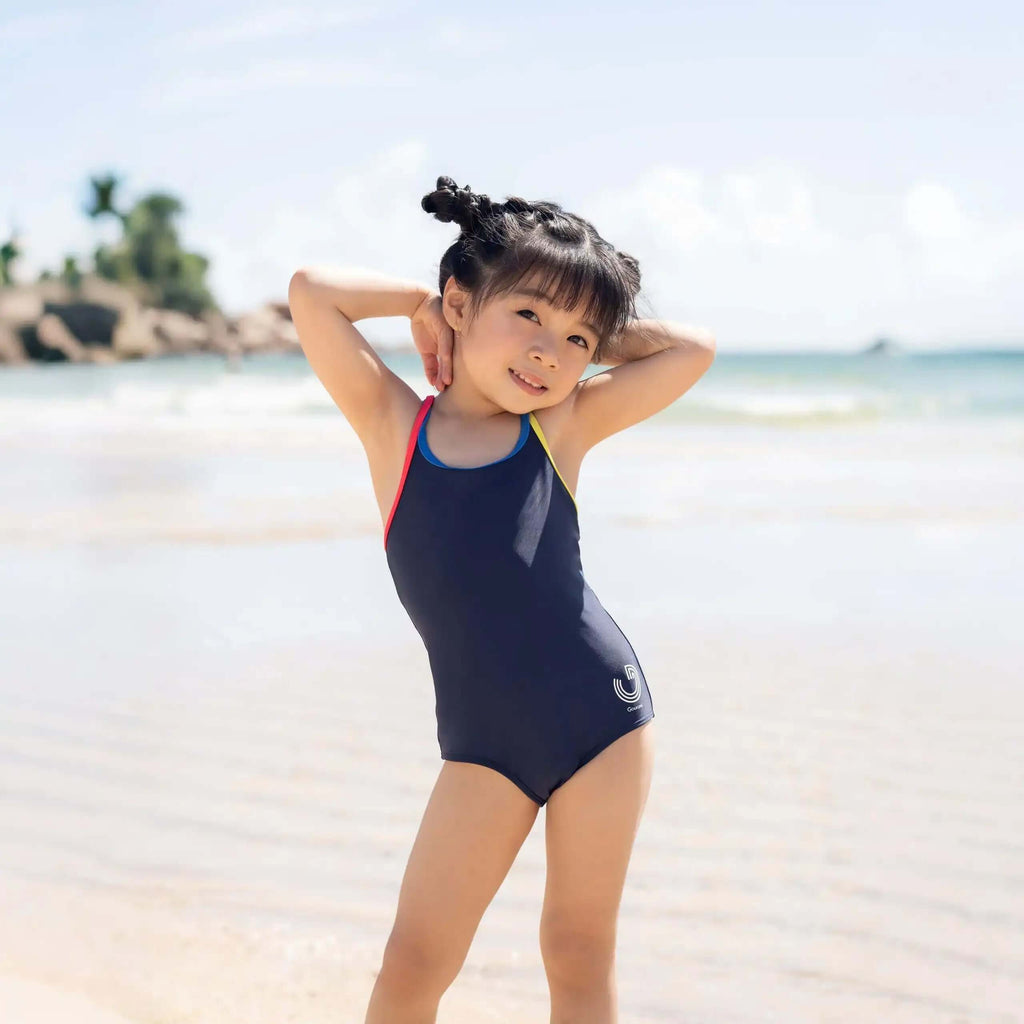Young girl in navy one-piece swimsuit posing on a sunny beach, kids swimwear fashion