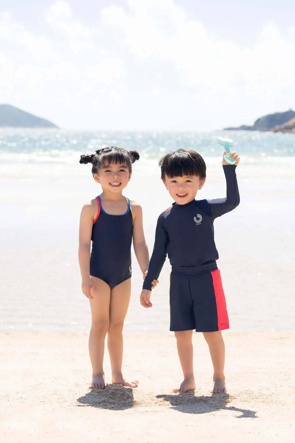穿着海军蓝泳装和运动服的孩子们在阳光明媚的海滩上微笑。