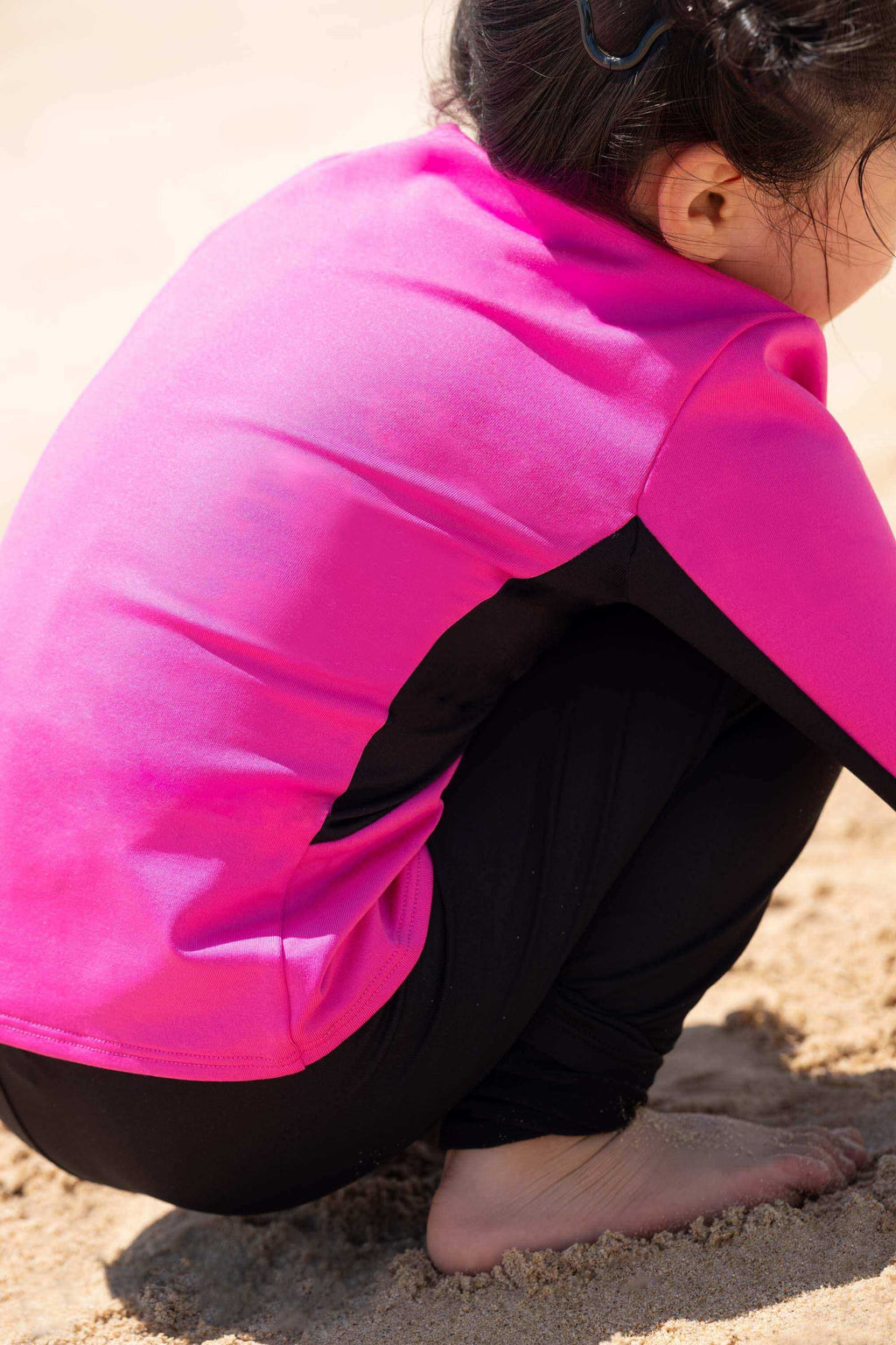 Child in pink and black long sleeve activewear crouching on sandy beach