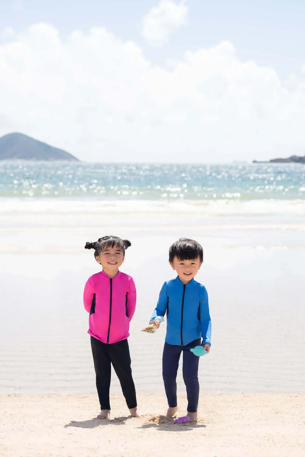 Two children in colorful long-sleeve swimwear playing on a sunny beach by the sea