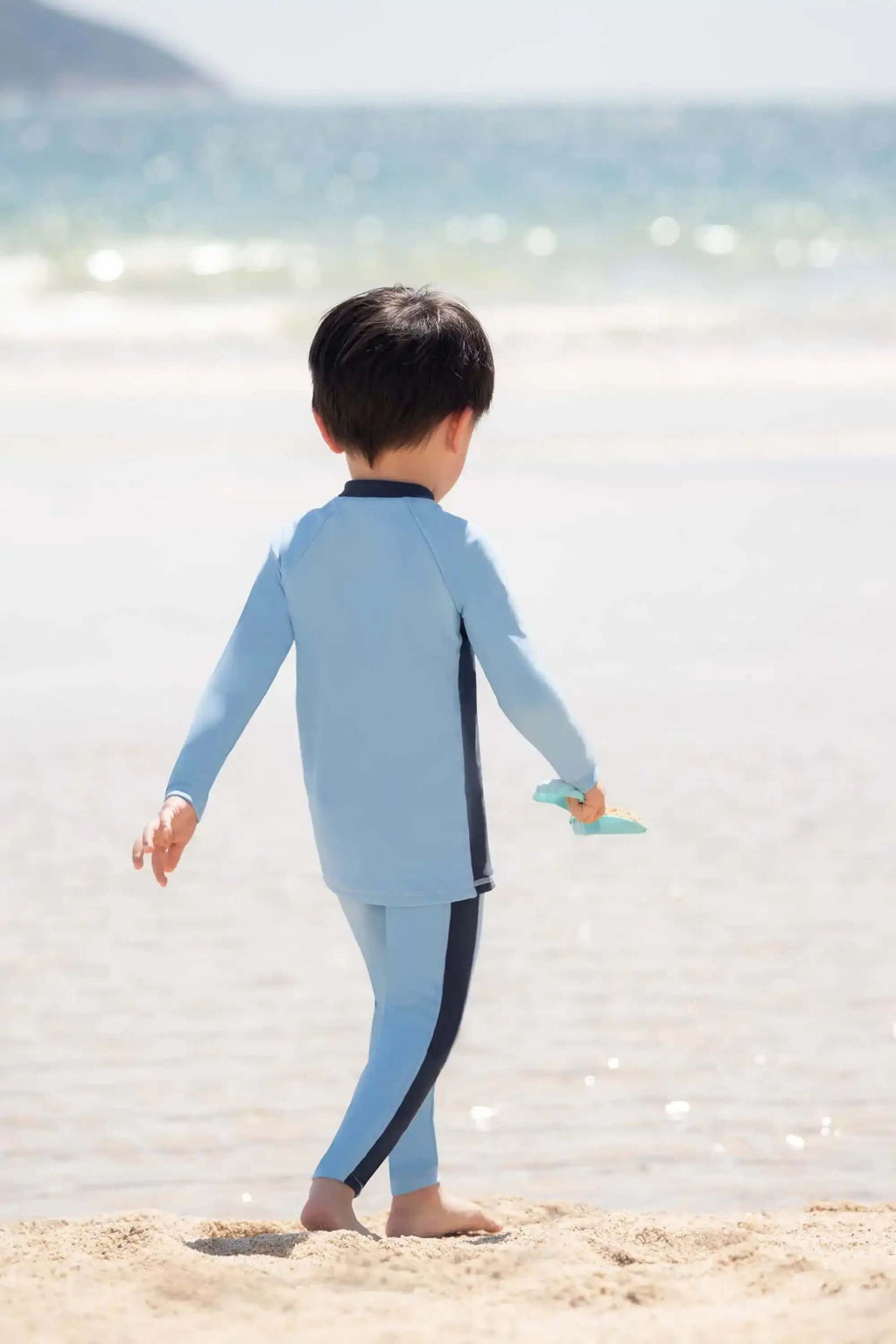 穿着浅蓝色长袖泳衣的孩子在海边的沙滩上玩耍